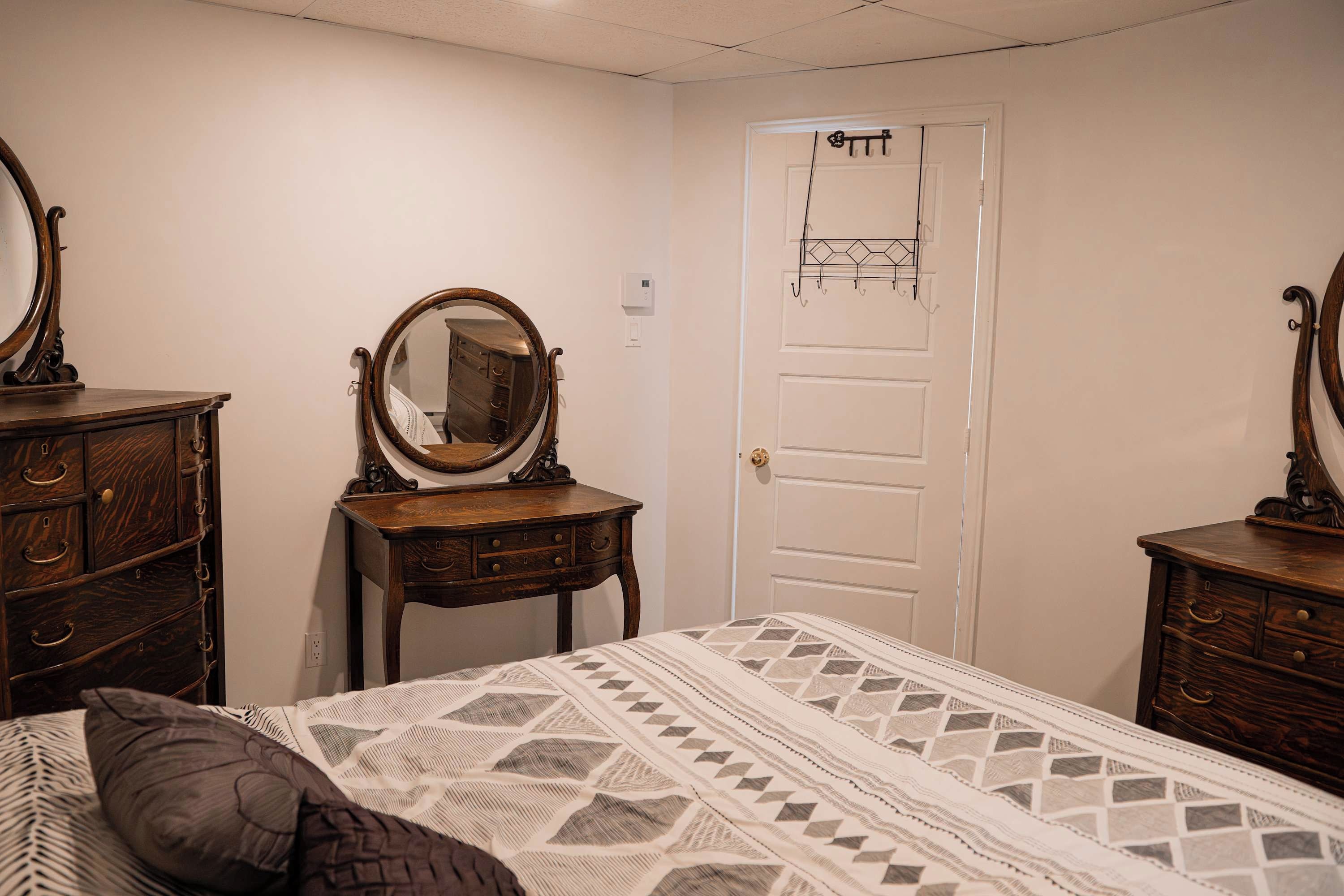 A bedroom with a bed, two wooden dressers, a dresser, a mirror, a door, and a wall-mounted light fixture.