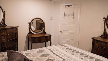 A bedroom with a bed, two wooden dressers, a dresser, a mirror, a door, and a wall-mounted light fixture.