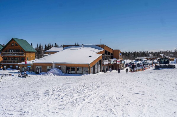 Un edificio cubierto de nieve con una amplia entrada de vidrio, fachada de madera y techo verde.