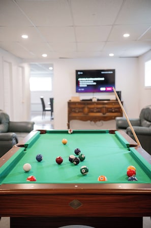 A pool table with balls in a room with a television in the background.