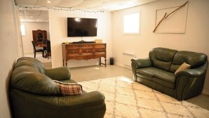 Uma sala de estar com dois sofás de couro, uma televisão de tela plana, um armário de madeira e um tapete felpudo.