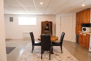A dining area with a round table and four chairs, a wooden cabinet with a microwave, and a window with blinds.