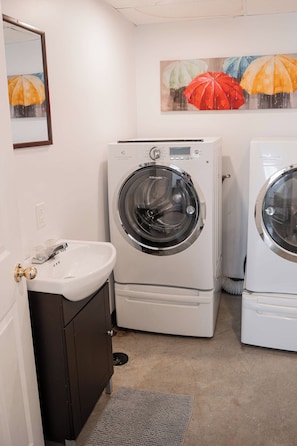A compact laundry room with two front-loading washing machines, a sink, and a cabinet.