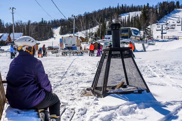 A ski resort with a chairlift, snow-covered ground, and a person sitting on a bench. - Lower Floor - Mont-Video (Barraute)
