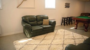 Um quarto com um sofá de couro verde, uma mesa de bilhar e um tapete branco e fofo.