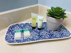Una bandeja con artículos de aseo como champú, acondicionador y jabón de baño, una planta en maceta y una bandeja estampada sobre una encimera de baño.