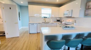 A modern kitchen with white cabinets, a built-in oven, and a central island with bar stools. - Beach House: Turtle’s Cove #3-Full Kitchen, Washer and Dryer, 1st Floor (Melbourne Beach)
