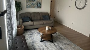 Ett vardagsrum med en soffa, ett runt soffbord, en klocka på väggen och en tavla.