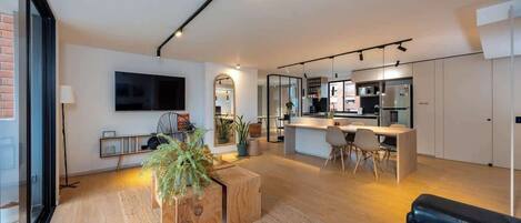 A modern living room with a large TV, a dining area, and a kitchen.