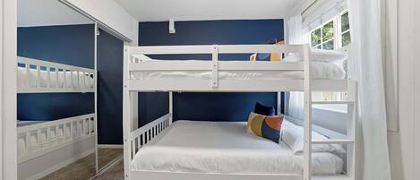 A bunk bed room with a lower bunk, a window with curtains, and a door with a mirror.