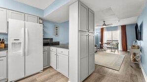 Een moderne keuken met witte kasten, een koelkast en een eethoek met een tafel en stoelen.