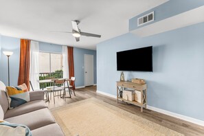 A living room with a sofa, TV, and a dining area with a table and chairs. - Cozy 3-bedroom condo on Okaloosa Island - Fort Walton Beach - with AC (Fort Walton Beach)