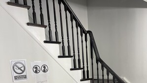 Eine Treppe mit schwarzen Spindeln, ein Glastisch mit einer gelben Schilder und zwei Rauchverbotsschildern an der Wand.