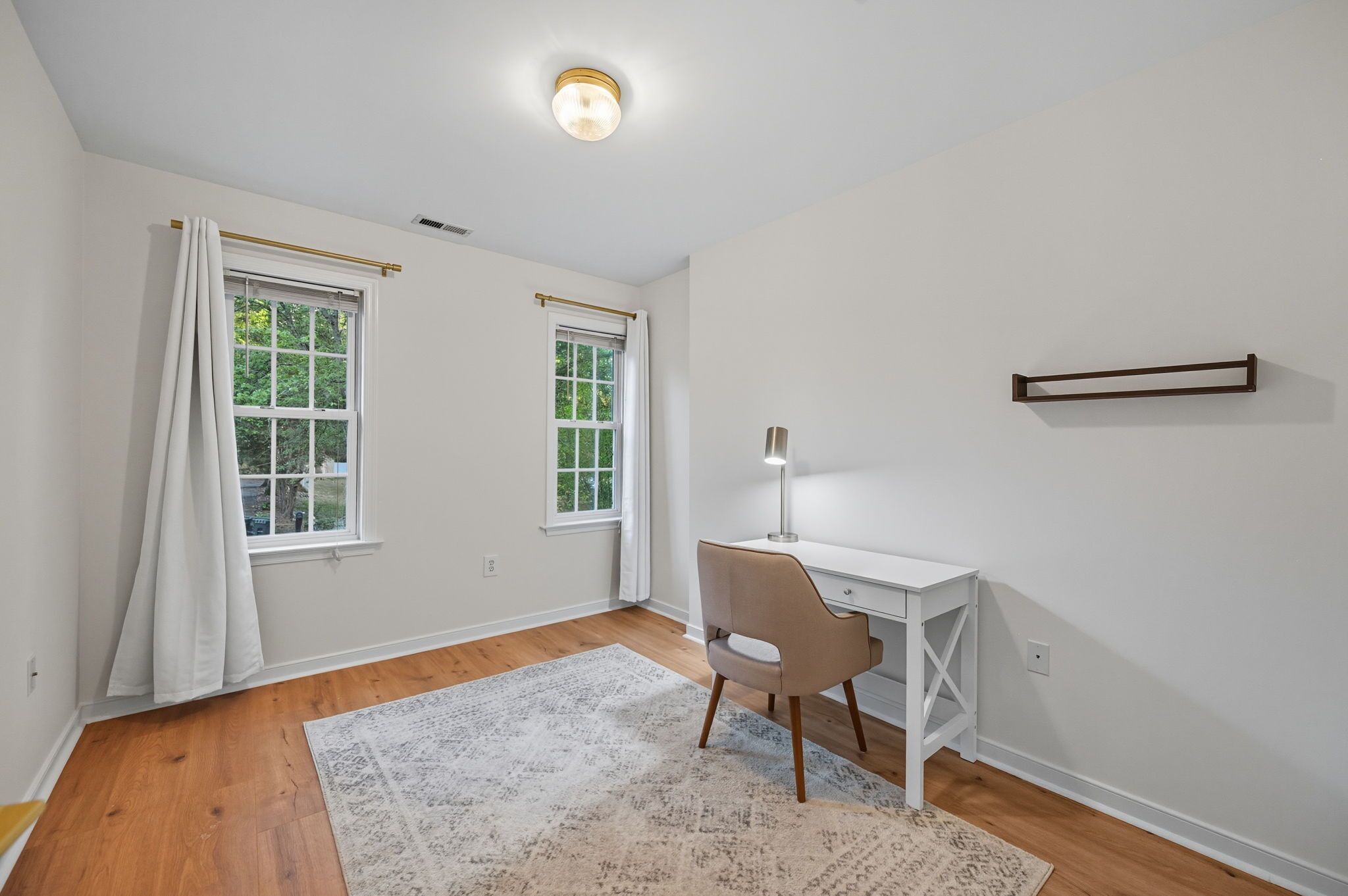 A room with two windows, a desk, a chair, and a rug.