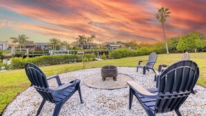 A patio with Adirondack chairs, a fire pit, and a view of a residential area with houses and palm trees. - Leaning Palm/Canal home/boat ramp & dock/game room + fire pit & lanai/sleeps 9 (Port Charlotte)