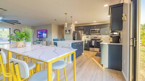 A modern kitchen with a central island, stainless steel appliances, and a dining area with yellow chairs. - Leaning Palm/Canal home/boat ramp & dock/game room + fire pit & lanai/sleeps 9 (Port Charlotte)