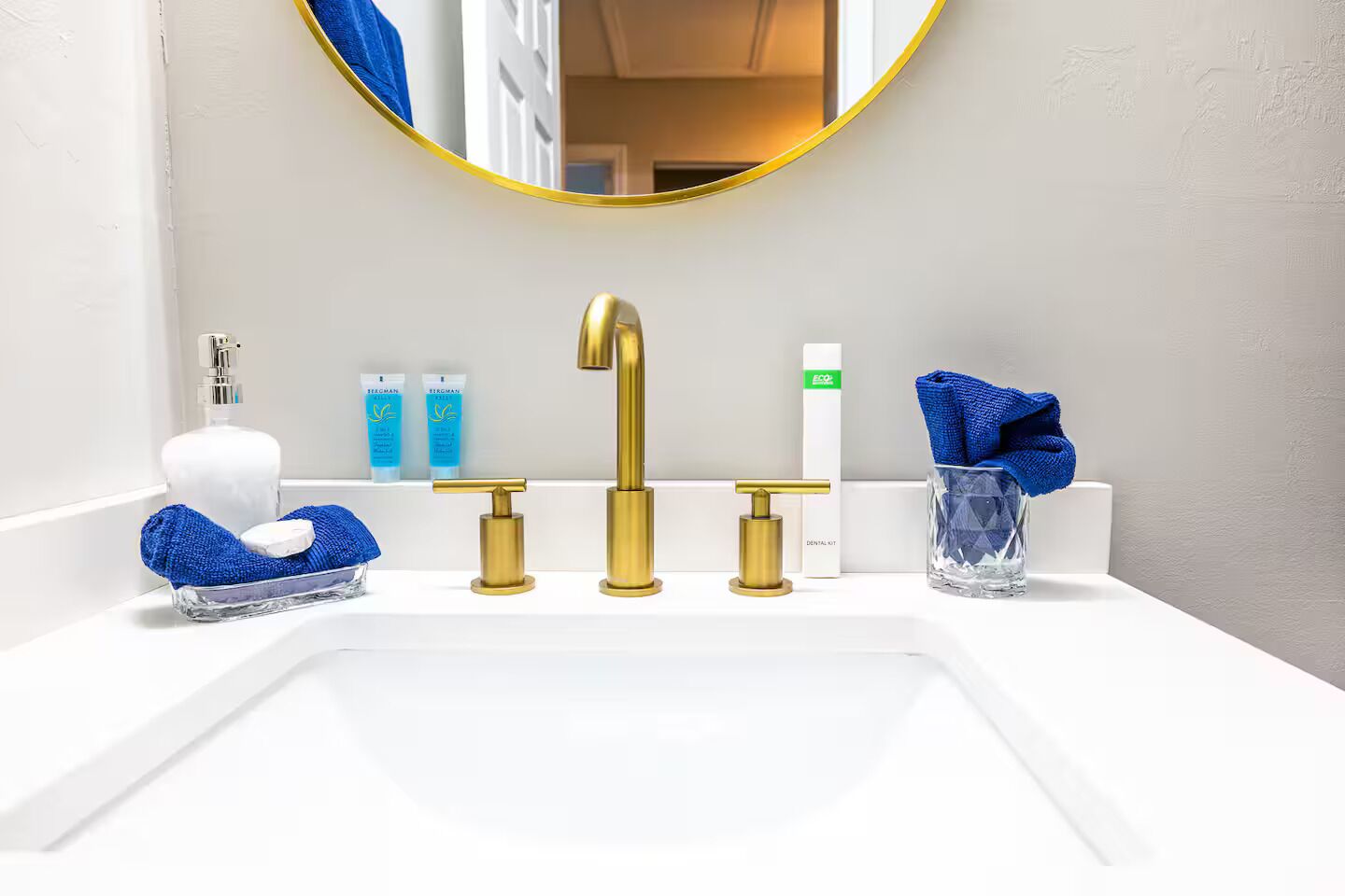 A bathroom with a white sink, gold faucets, a blue towel, and a glass jar with a blue towel.