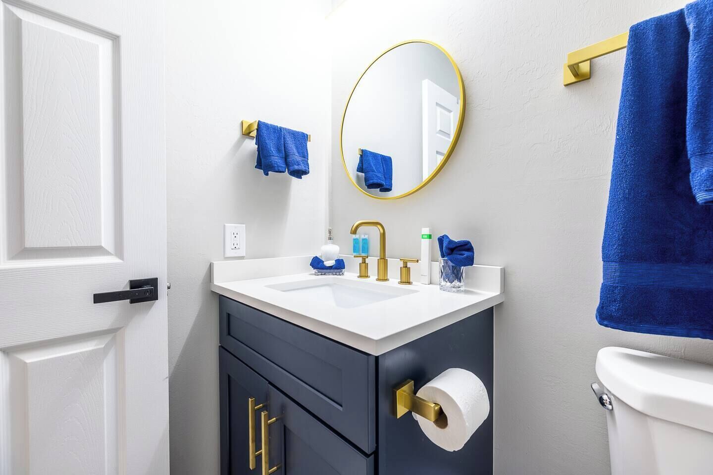A bathroom with a white sink, gold faucets, a dark cabinet, a toilet, and a mirror with a gold frame.