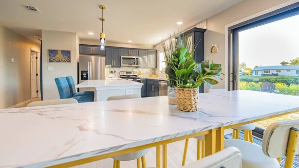 A modern kitchen with a central island, stainless steel appliances, and a large window offering a view of the outdoors. - Leaning Palm/Canal home/boat ramp & dock/game room + fire pit & lanai/sleeps 9 (Port Charlotte)