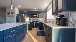 A modern kitchen with dark blue cabinets, stainless steel appliances, and a marble backsplash. - Leaning Palm/Canal home/boat ramp & dock/game room + fire pit & lanai/sleeps 9 (Port Charlotte)