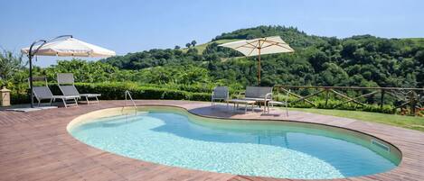 A swimming pool with wooden decking, lounge chairs, and umbrellas.