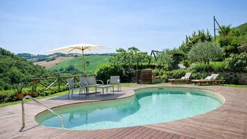 Un patio in legno con piscina, poltrona a sdraio e ombrellone.