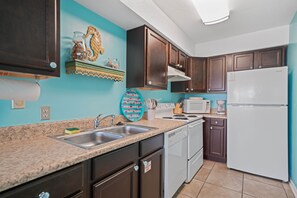 A kitchen with dark wooden cabinets, a white refrigerator, a microwave, and a stove. - Deja Blue: Navarre Beach (Navarre)