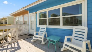 Ein blaues Haus mit weiß gefassten Fenstern, eine Veranda mit weißen Schaukelstühlen und einem kleinen grünen Tisch.