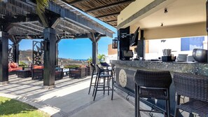 Eine Außenbar mit Korbmöbeln, Blick auf den Ozean und einer Pergola.