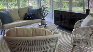 Une véranda avec un canapé, des fauteuils en osier, une table basse et une cheminée.