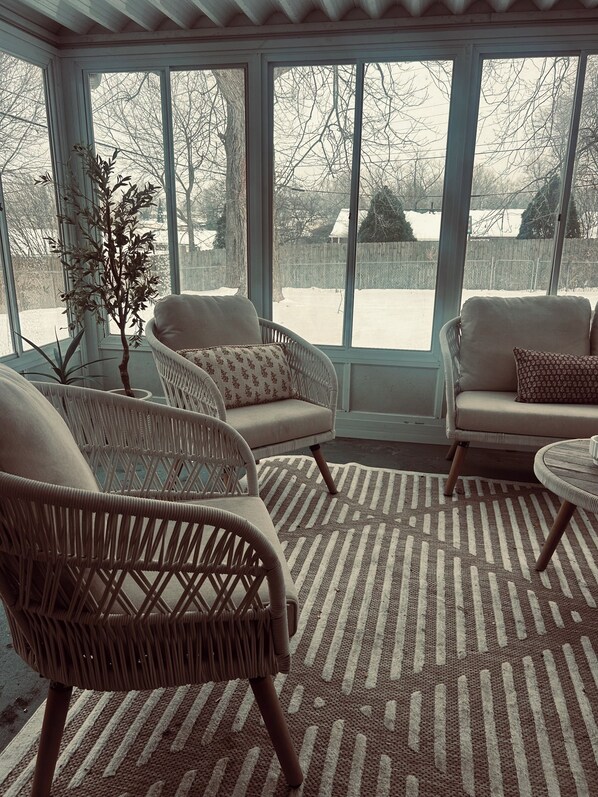 A sunroom with wicker chairs, a patterned rug, and a view of a snowy yard. - King suite + Hot Tub near the Greene (Dayton)