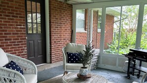 Eine überdachte Veranda mit Korbmöbeln, einem kleinen Tisch mit Pflanze und einem Grill.