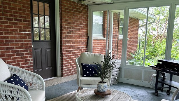 Een overdekt terras met rieten meubilair, een kleine tafel met een plant en een barbecue.