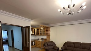 Un vaste salon doté d’un parquet, d’un canapé en cuir marron, d’un fauteuil en cuir et d’un coin repas avec des meubles de rangement en bois et un lustre.