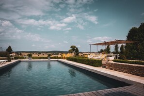 Ein rechteckiger Pool mit Holzterrasse, umgeben von weißen Liegestühlen und einer Pergola.