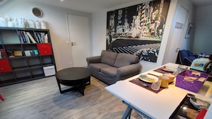 A modern living room with a grey sofa, a round coffee table, and a dining table with a purple basket. There is a bookshelf with red and black shelves and a cityscape painting on the wall. - Les nichoirs - 60m² room in Vouvray - bathroom and separate toilet (Vouvray)