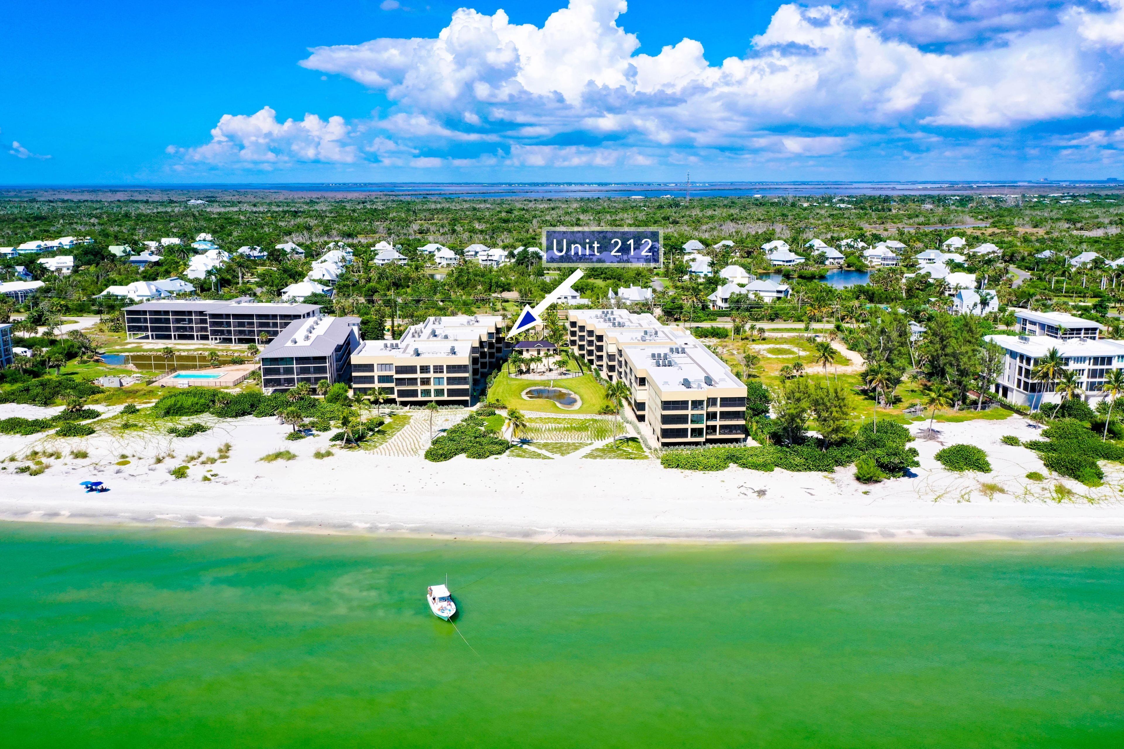 An aerial view of a coastal residential area with multiple buildings, a clear blue sky, and a boat on the water.
