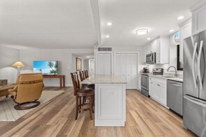 A modern kitchen with white cabinets, a stainless steel refrigerator, and a dining area with a wooden table and chairs. - Beachfront Condo on West Gulf Drive with Stunning Gulf Views (Sanibel)