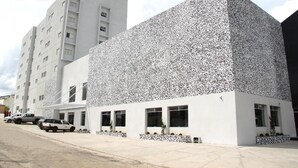 Un hotel moderno con una fachada distintiva cubierta por un patrón texturizado, un estacionamiento y un cielo despejado.