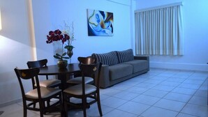 Una sala de estar con un sofá gris, una mesa de comedor con sillas, un florero con flores y un cuadro en la pared.