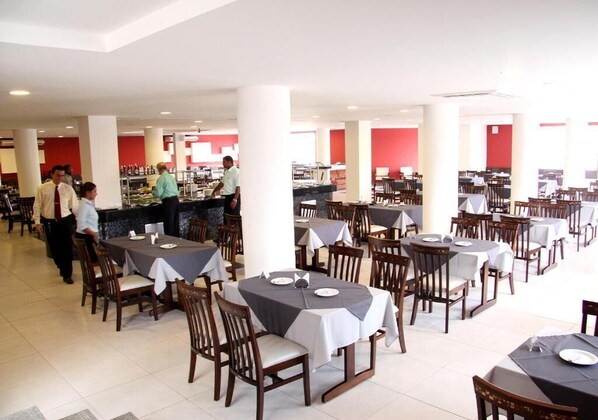 A spacious restaurant with multiple tables and chairs, a bar area, and a bright interior. - Hotel Aster  (Alagoinhas)