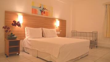 A hotel room with a large bed, two bedside lamps, a wooden headboard, a small bedside table with a vase of flowers, and a radiator.