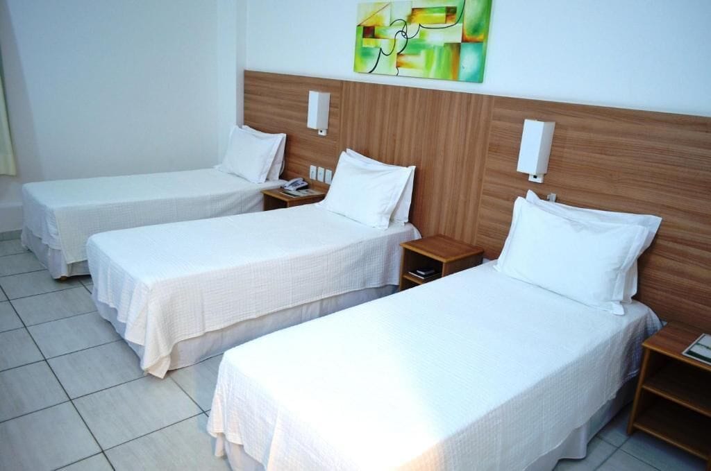 A hotel room with two single beds, each with a wooden headboard, white bedding, and bedside tables with lamps.