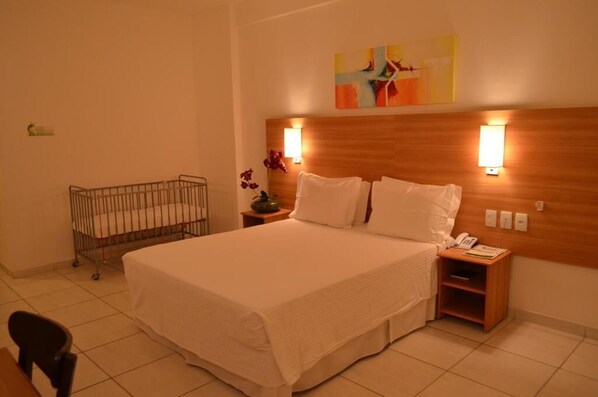 A hotel room with a large bed, two bedside tables, a wall-mounted artwork, and a crib. - Hotel Aster  (Alagoinhas)