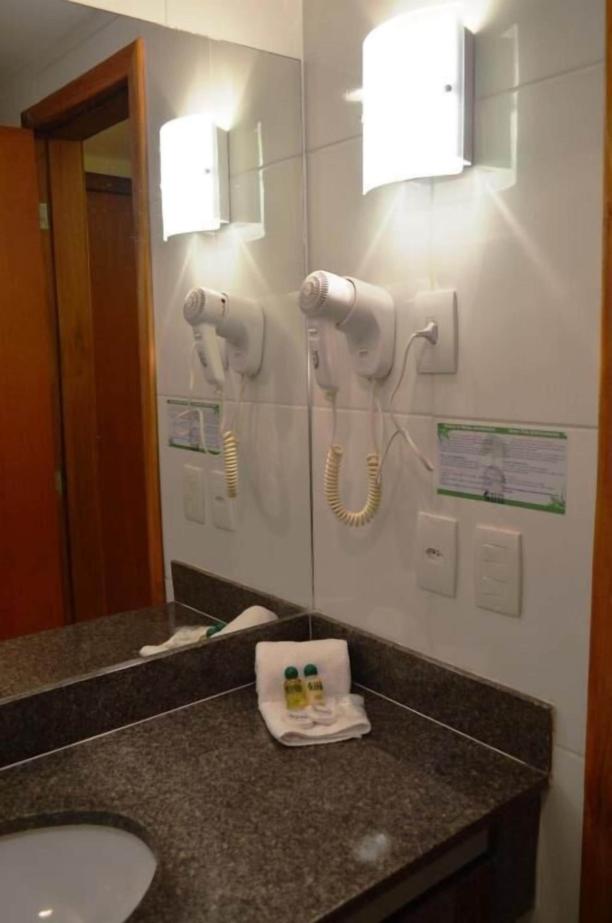 Ein Badezimmer mit einer Granit-Arbeitsplatte, einem Spiegel, einem Handtuchhalter mit Handtuch und zwei an der Wand befestigten Haartrocknern.