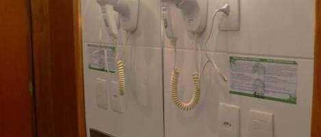 A bathroom with a granite countertop, a mirror, a towel rack with a towel, and two hair dryers mounted on the wall.