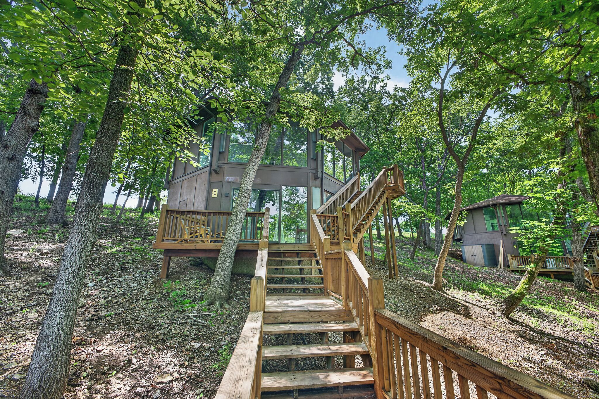 A wooden staircase leading to a treehouse with a balcony, surrounded by dense forest.