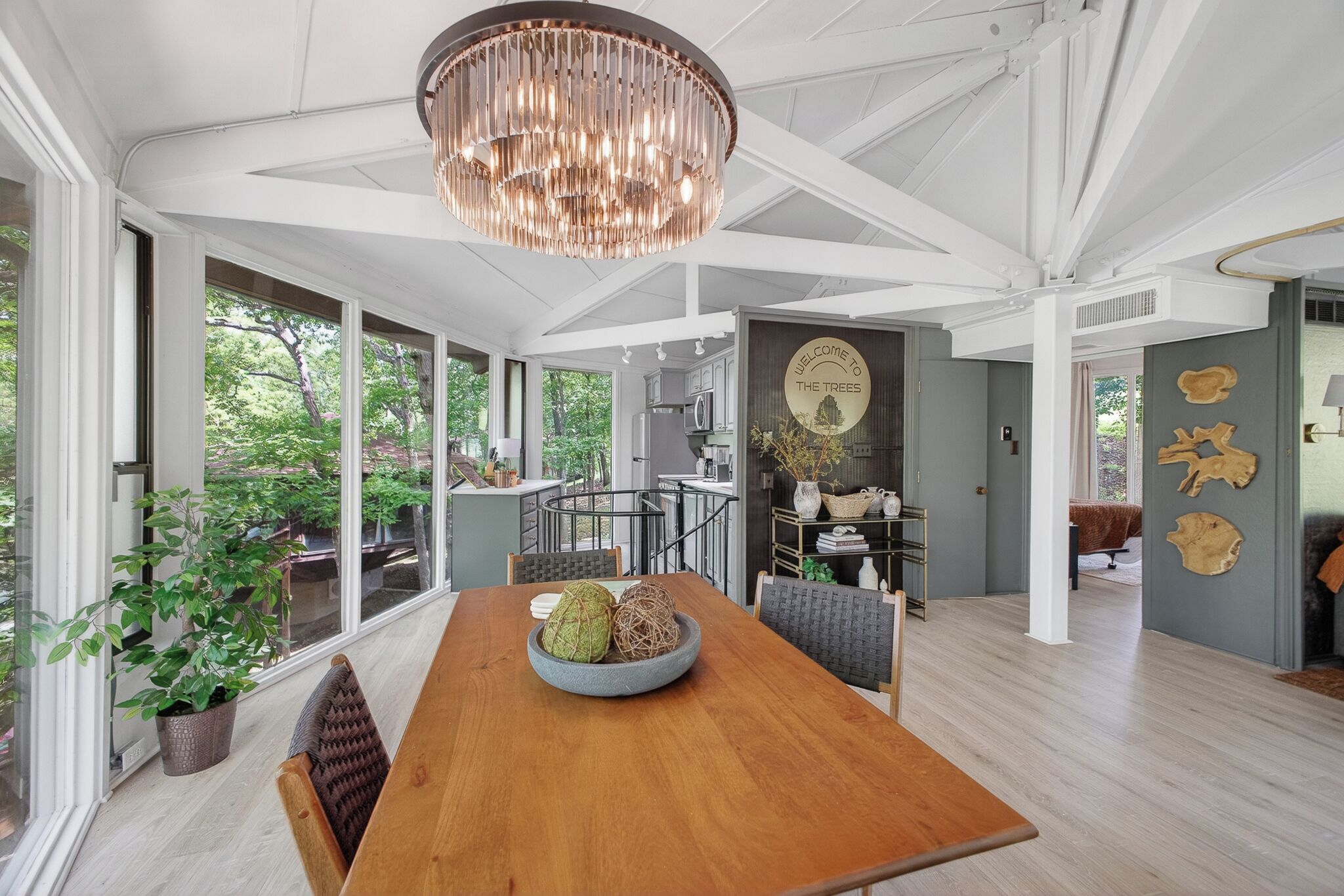 A spacious dining area with a wooden table, a chandelier, and a view of the outdoors through large windows.