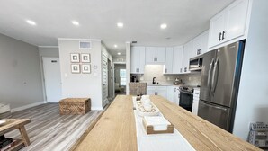 Una cocina moderna con armarios blancos, una isla de madera, electrodomésticos de acero inoxidable y un letrero que dice 'RELAX'.
