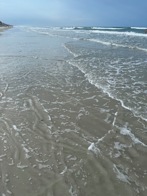 A beach with waves, buildings in the background, and a clear sky.